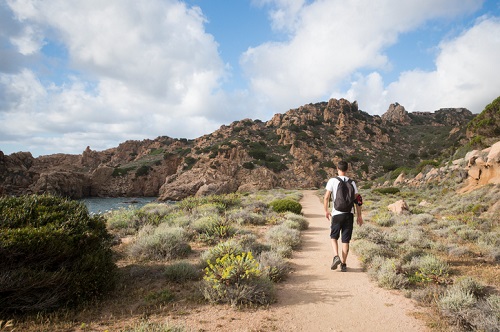 A man with a backpack is hiking along the trail coast of Sardinia in Italy