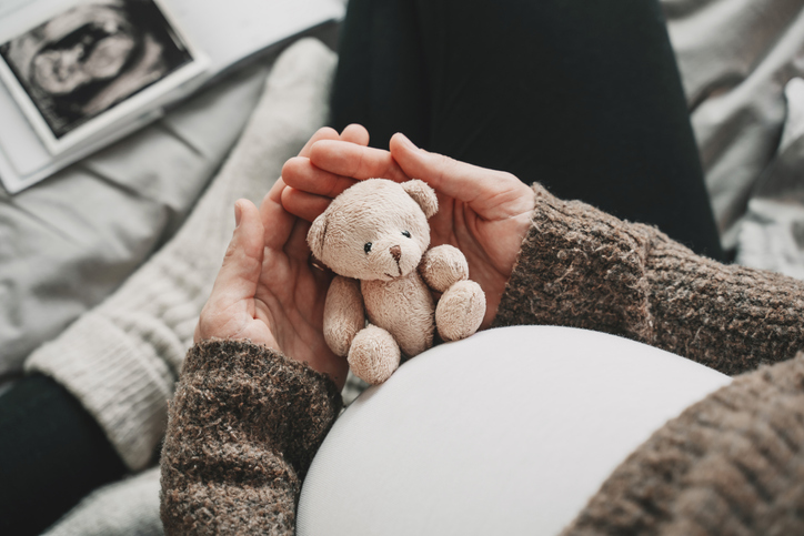 Woman pregnant belly with little teddy toy bear. Concept image with symbol of many meanings for expectant mother during pregnancy and her unborn baby.