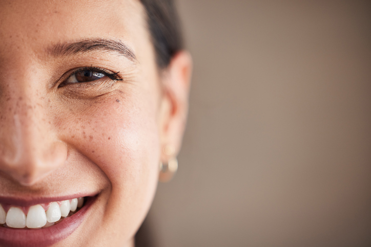Face of beautiful mixed race woman smiling with white teeth.  Portrait of a woman’s face with brown eyes and freckles posing with copy-space. Dental health and oral hygiene